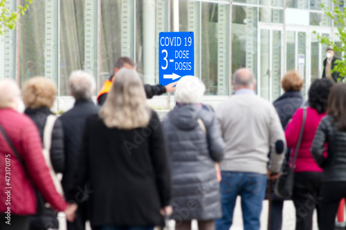 people queue draggle to receive the third dose of the coronavirus covid 19 vaccine , signal in spanish and english languaje