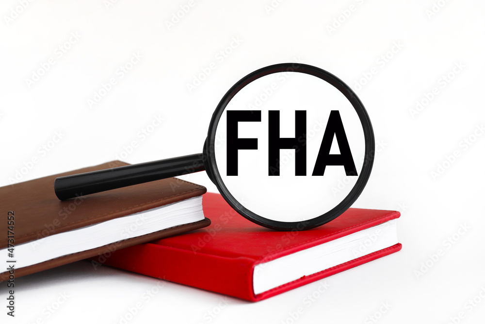 FHA. white background text on magnifying glass. magnifying glass on brown and red notebook FHA. white background text on magnifying glass. magnifying glass on brown and red notebook
