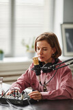 Vertical portrait of young woman speaking to microphone while recording podcast in studio