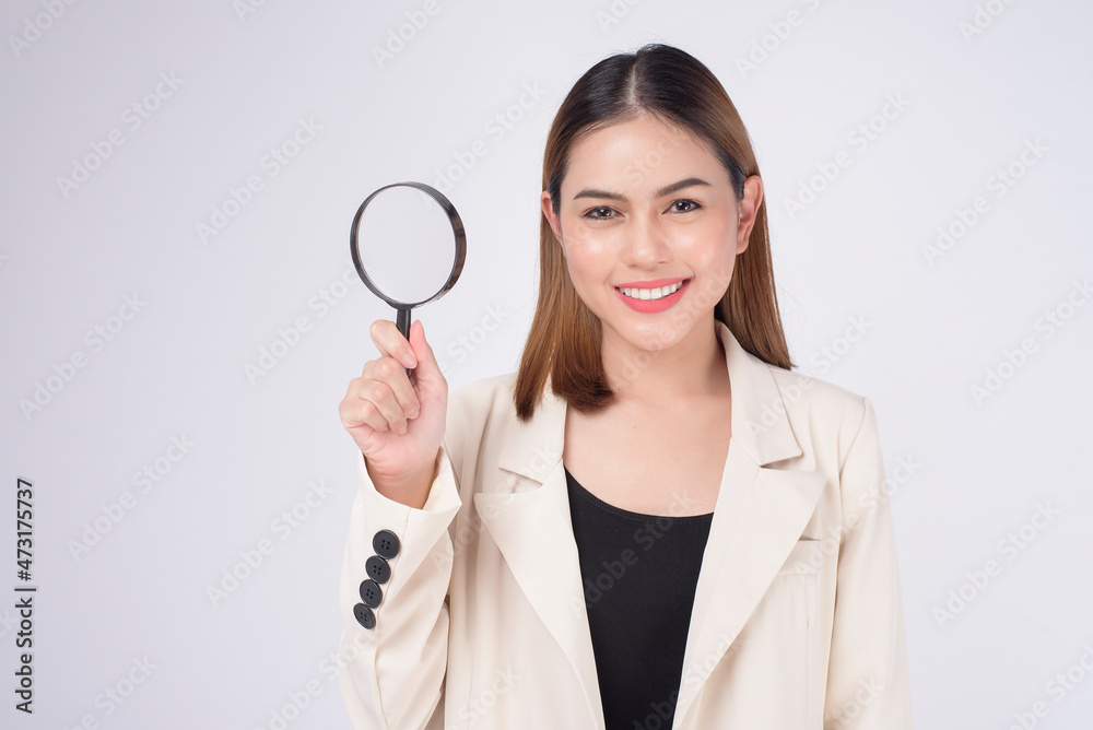 Young beautiful woman in suit holding magnifying glass over white background studio Young beautiful woman in suit holding magnifying glass over white background studio