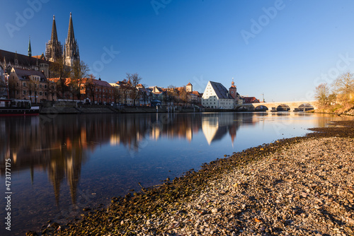 Donauufer in Regensburg mit Dom  Spiegelungen und steinerner Br  cke bei blauem Himmel   im Abendlicht im Winter