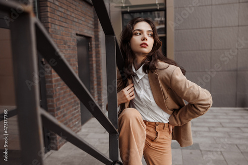  Tall stylish girl with oversized jacket posing near the railing and steps on the city background photo