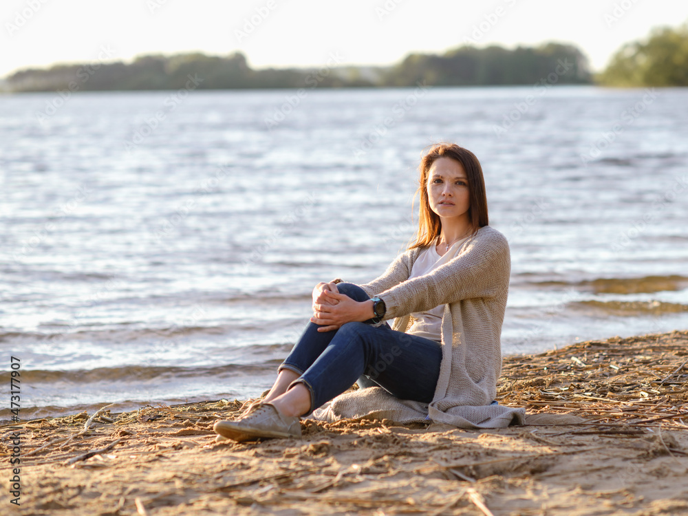 fashionable girl in trousers, blouse walks on the shore of the lake. sunset. girl resting on the seashore