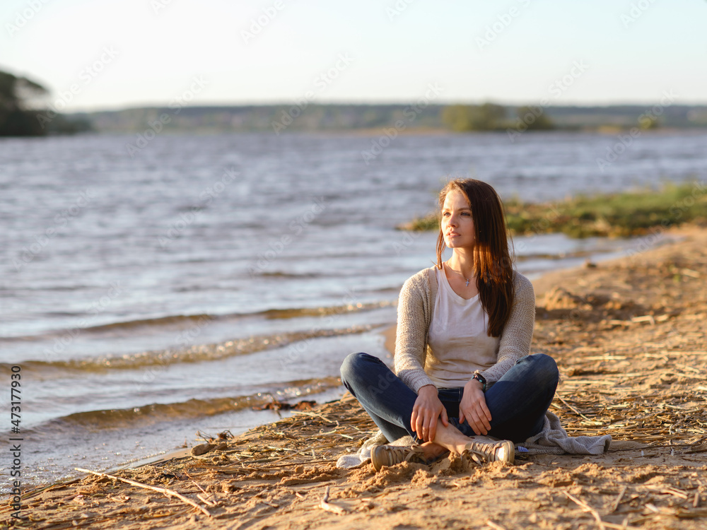 fashionable girl in trousers, blouse walks on the shore of the lake. sunset. girl resting on the seashore