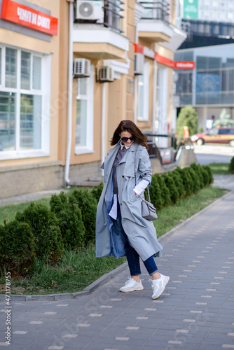 a fashionable girl in trousers, a raincoat, a blouse with a handbag walks around the city. Business concept