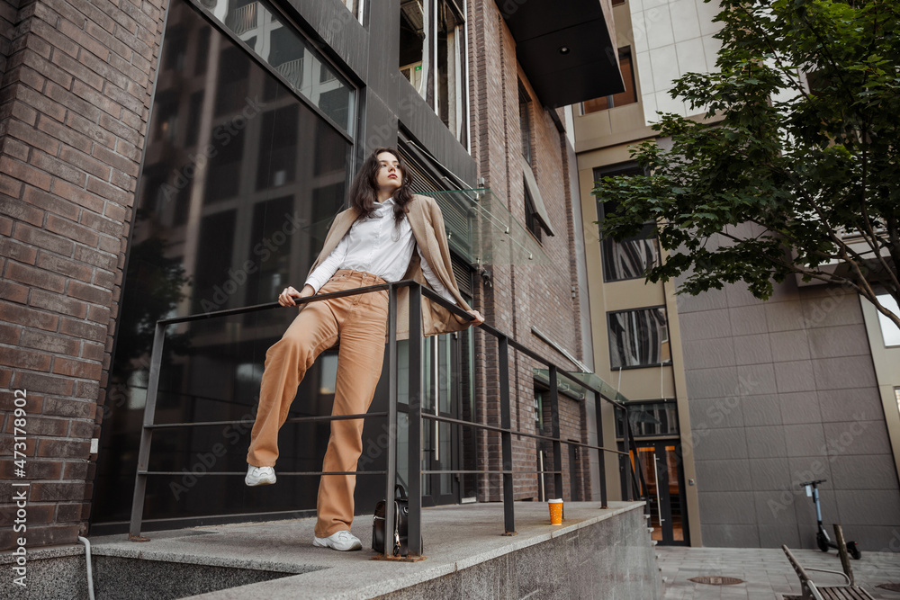  Tall stylish girl with oversized jacket posing near the railing and steps on the city background