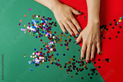 Festive manicure with confetti and glitter on a Christmas background. Colored nail polish with sequins