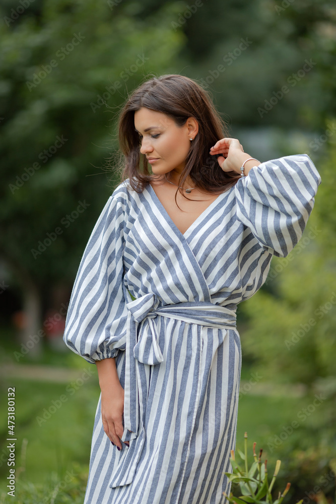 Portrait of a beautiful brunette in a striped dress in a summer garden. High quality photo Portrait of a beautiful brunette in a striped dress in a summer garden. High quality photo