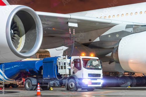 Truck with a tank of kerosene of aviation fuel connected to the fuel tanks of a large aircraft airliner, refueling service of a night flight. photo