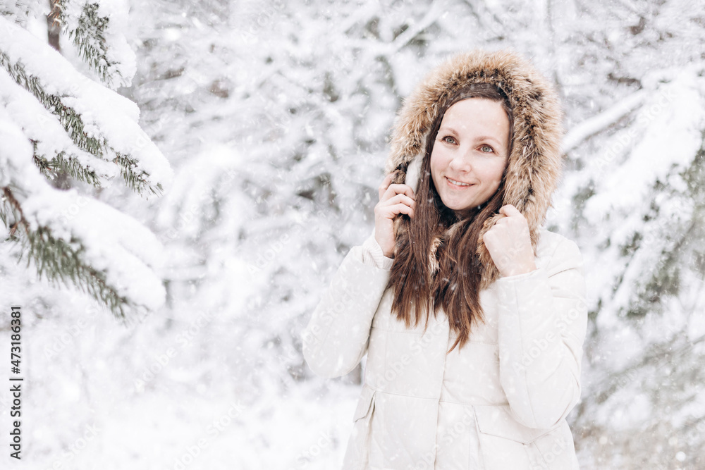 Winter portrait of young woman. Happy girl walking in winter forest and looking snow falling down. Christmas and New year holidays. Slow life. Cute lady in warm clothing having fun in nature outdoors. Winter portrait of young woman. Happy girl walking in winter forest and looking snow falling down. Christmas and New year holidays. Slow life. Cute lady in warm clothing having fun in nature outdoors.