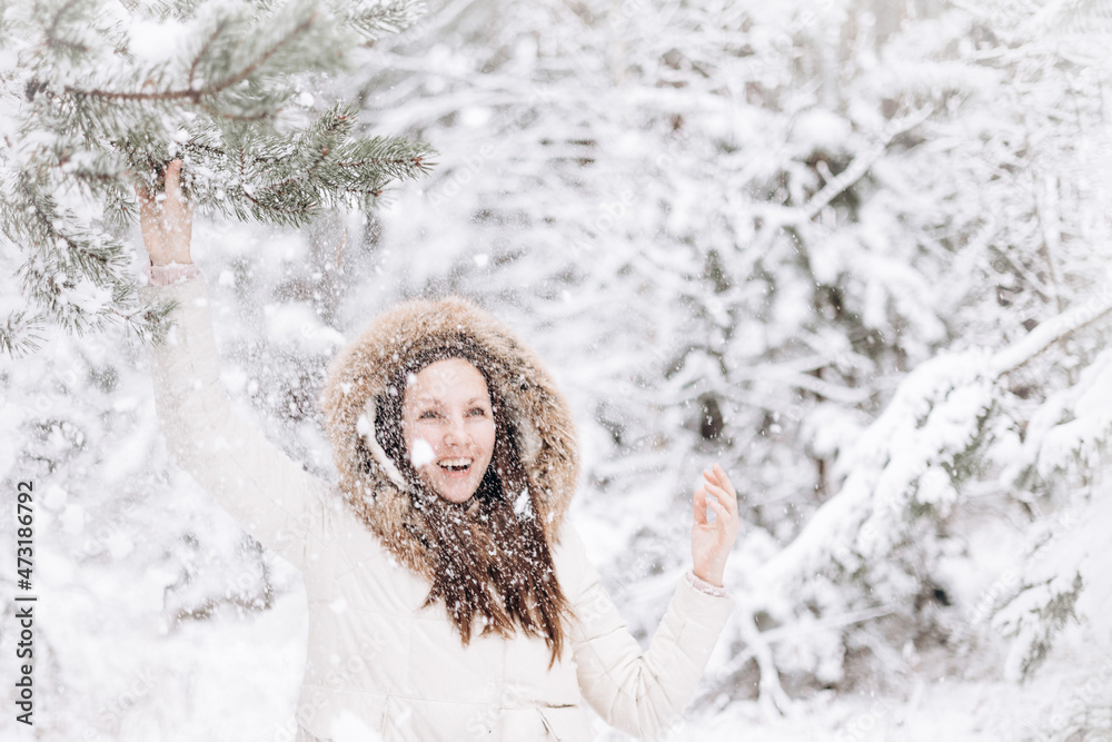 Winter portrait of young woman. Happy girl walking in winter forest and looking snow falling down. Christmas and New year holidays. Slow life. Cute lady in warm clothing having fun in nature outdoors. Winter portrait of young woman. Happy girl walking in winter forest and looking snow falling down. Christmas and New year holidays. Slow life. Cute lady in warm clothing having fun in nature outdoors.