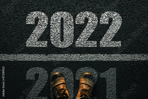 Men's feet in boots on the pavement transcend 2021 and go into 2022. New Year's 2022 Concept. White numbers 2022 on asphalt, top view