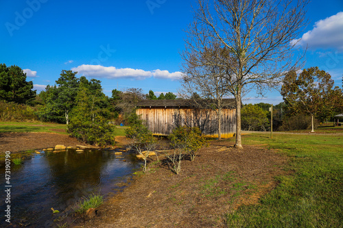 a shot of a creek in the park with a wooden covered bridge surrounded by lush green and autumn colored trees and grass with blue sky at Garrard Landing Park in Alpharetta Georgia USA photo