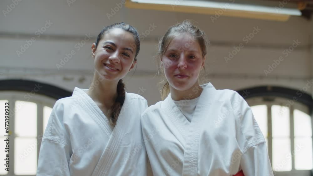 Front view of happy Caucasian girls in kimono looking at camera. Medium shot of smiling and beautiful martial artsists standing in gym after karate training, posing for camera. Emotion, sport concept Front view of happy Caucasian girls in kimono looking at camera. Medium shot of smiling and beautiful martial artsists standing in gym after karate training, posing for camera. Emotion, sport concept