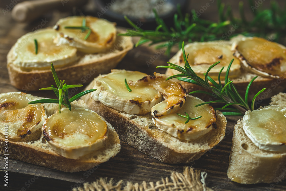 Baguette bread slices baked with goat cheese and honey, decorated with rosemary, on wooden background Baguette bread slices baked with goat cheese and honey, decorated with rosemary, on wooden background