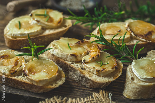 Baguette bread slices baked with goat cheese and honey, decorated with rosemary, on wooden background
