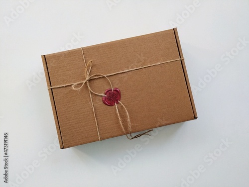 Brown gift box with twine bow and  burgundy wax seal lies on white table