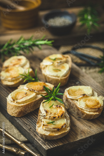 Baguette bread slices baked with goat cheese and honey on wooden background, vertical