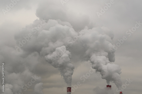 exhaust from industrial pipes from a production or thermal power plant. Steam or polluted smoke escapes from the pipes into the gray cloudy sky