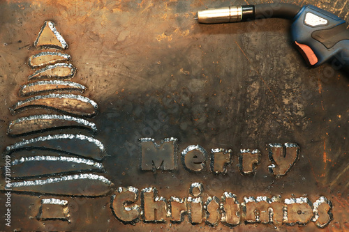 A steel sheet of metal on which a Christmas tree is welded and the phrase Merry Christmas. Christmas card for workers in heavy industry and metalworking. 