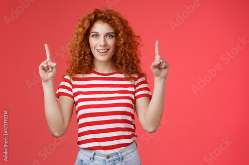 Excited good-looking cheeky redhead ginger girl curly natural hair pointing raised index fingers up smiling impressed thrilled advising store directing promo advertising awesome haircare product photo