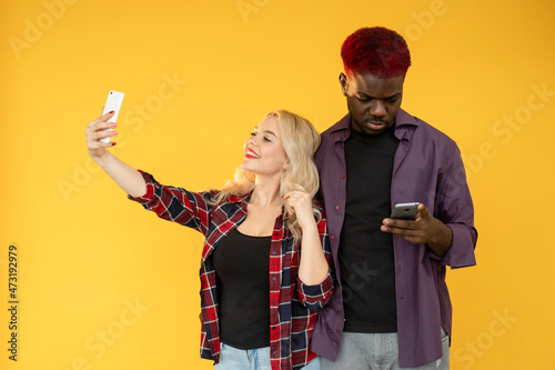 Different personality. People diversity. Introvert extrovert. Millennial lifestyle. Multiracial friends happy woman taking selfie Afro man using cell isolated on orange background. photo