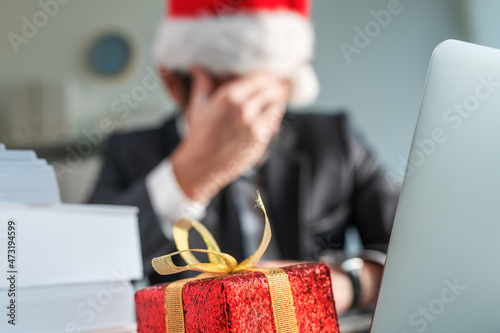 Sad and unhappy businessman with Santa Claus hat crying in office during Christmas holiday season photo