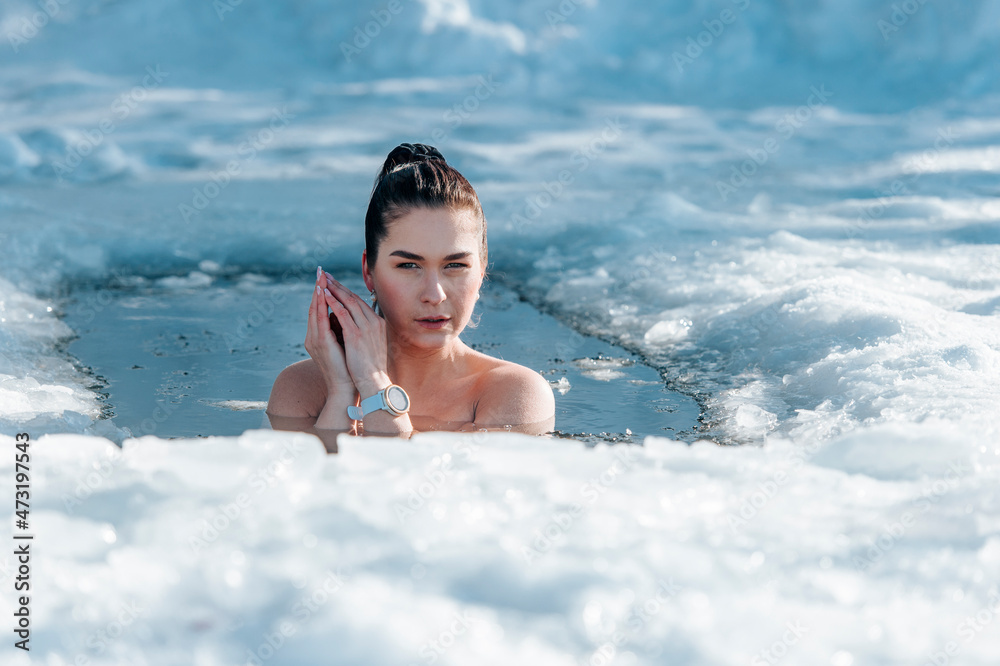 Girl with bikini and a watch in frozen lake ice hole. Woman hardening the  body in cold water. Good immunity is protection against many diseases.  Vintage color filter foto de Stock