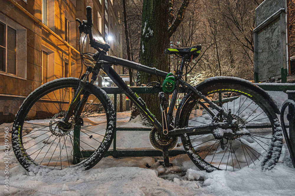 snow-covered bike near an apartment building at night during a snowfall