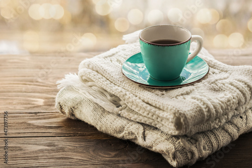 A cup of coffee on a stack of cozy knitted scarves in pastel colors on a wooden background. Morning cozy coffee. Copy space.
