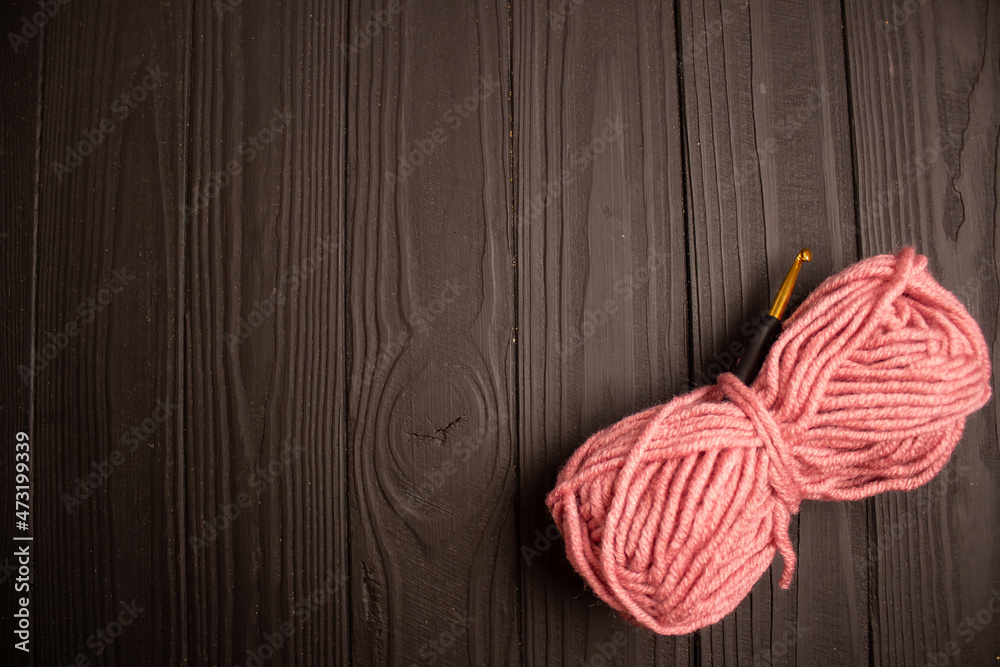 pink yarn and crochet hook on dark wooden background