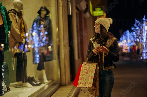 Woman at Christmas shopping using phone and looking in the shop window