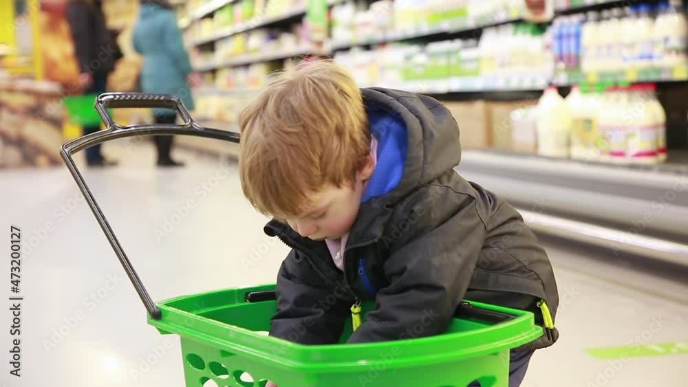 A little boy Checks the Contents of the Basket, groceries, purchases and gifts. The background is blurred. The background is blurred A little boy Checks the Contents of the Basket, groceries, purchases and gifts. The background is blurred. The background is blurred