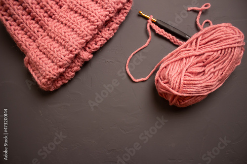 warm hat, yarn crochet and skeins of pink thread on a gray background