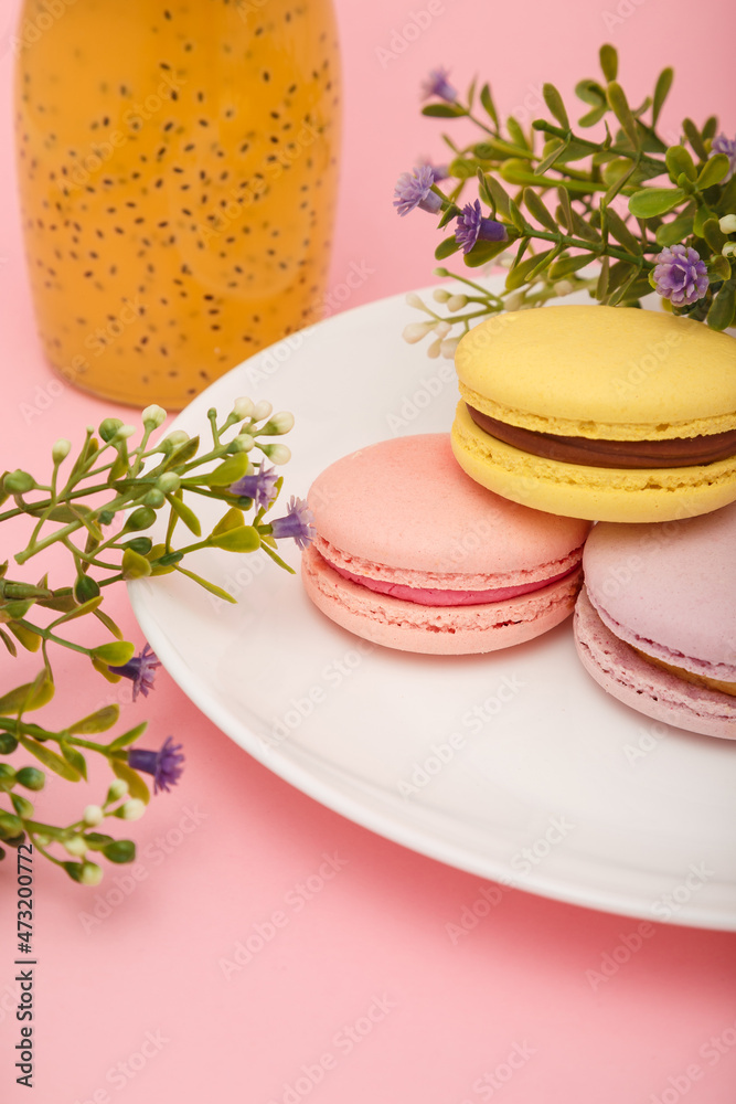 Plate of macaroons on pink background with flowers. Drink in bottle. Sweet pastry, baked products, sweets, dessert. Plate of macaroons on pink background with flowers. Drink in bottle. Sweet pastry, baked products, sweets, dessert.