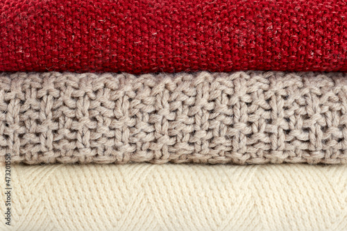 Background from warm knitted sweaters. A stack of red, beige and white sweaters close up. Stylish clothes for the cold season
