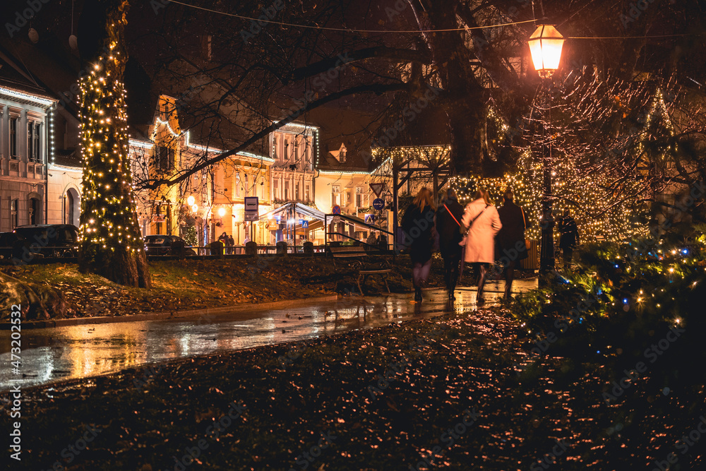 Street lamps shining light on the passing people during rainy, cold winter evening in the beautiful town of Samobor
