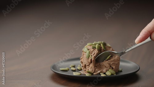 man eat chocolate ice cream with punpkin seeds on small saucer on wood table