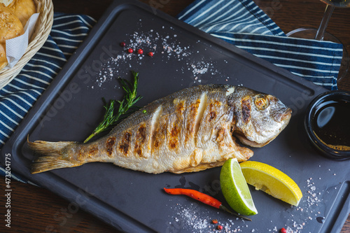 Grilled fish on a plate with a glass of wine and baked vegetables.