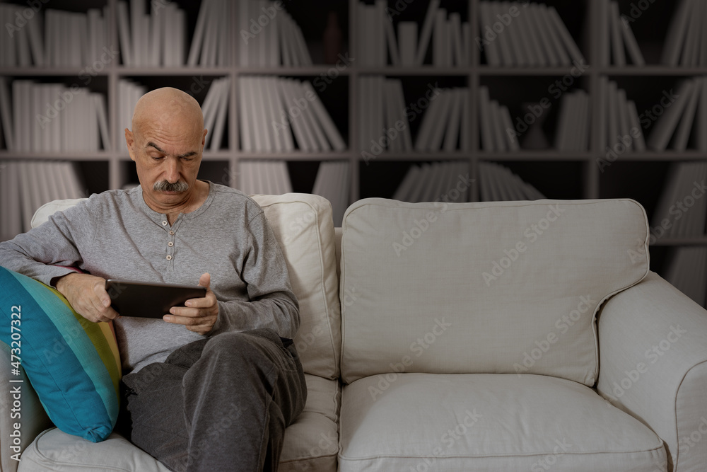 Senior Male Reading in a Digital Tablet Sitting at the Sofa at the House Living Room