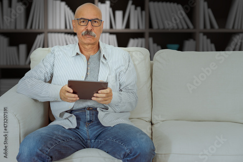 Senior Male Reading in a Digital Tablet Sitting at the Sofa at the House Living Room