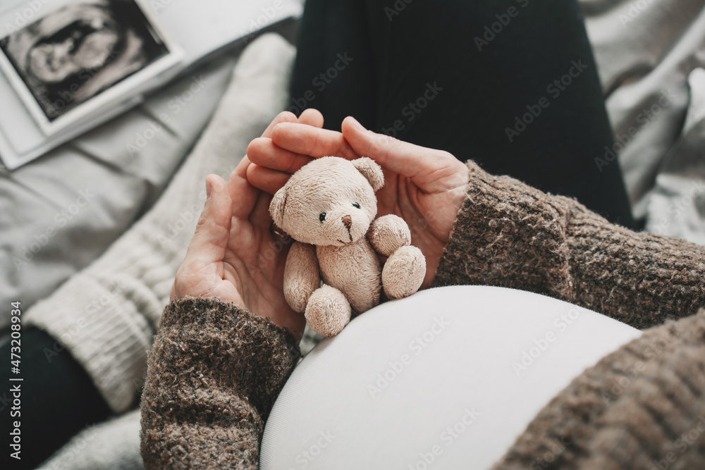 Woman pregnant belly with little teddy toy bear. Concept photo with symbol of many meanings for expectant mother during pregnancy and her unborn baby. - obrazy, fototapety, plakaty 