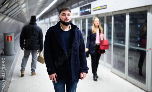 Young bearded man waiting for subway train, walking at modern underground station