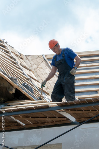 Repair of an old wooden roof. Replacement of tiles and wooden beams in an old house. A carpenter with tools in his hands is on the roof of the building during the work.