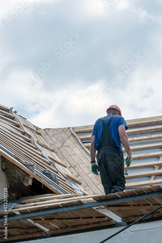 Repair of an old wooden roof. Replacement of tiles and wooden beams in an old house. A carpenter with tools in his hands is on the roof of the building during the work.