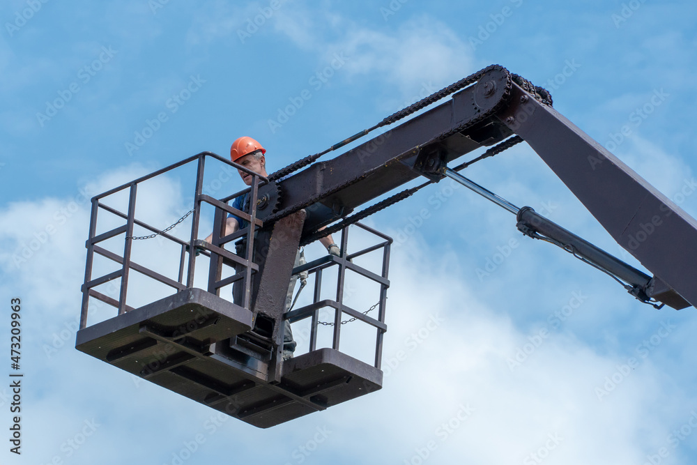 A special platform for lifting builders to a height to work on the repair and maintenance of building facades against the blue sky. A basket or cradle for people that is lifted by a crane. A special platform for lifting builders to a height to work on the repair and maintenance of building facades against the blue sky. A basket or cradle for people that is lifted by a crane.