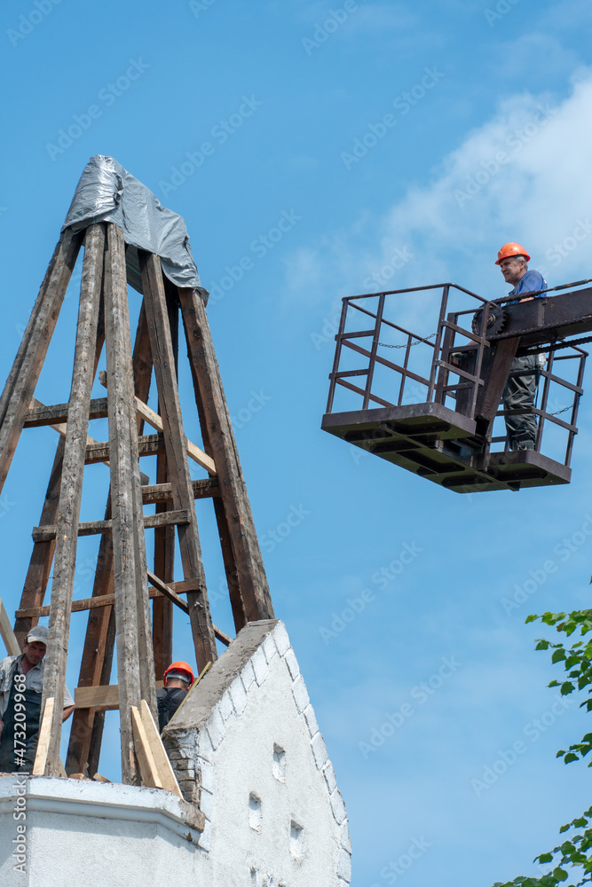 Repair of the old wooden roof of a beautiful historical building. The crane lifts the builders to a height on a special cradle or basket to perform the work. Carpenter on the roof. Repair of the old wooden roof of a beautiful historical building. The crane lifts the builders to a height on a special cradle or basket to perform the work. Carpenter on the roof.