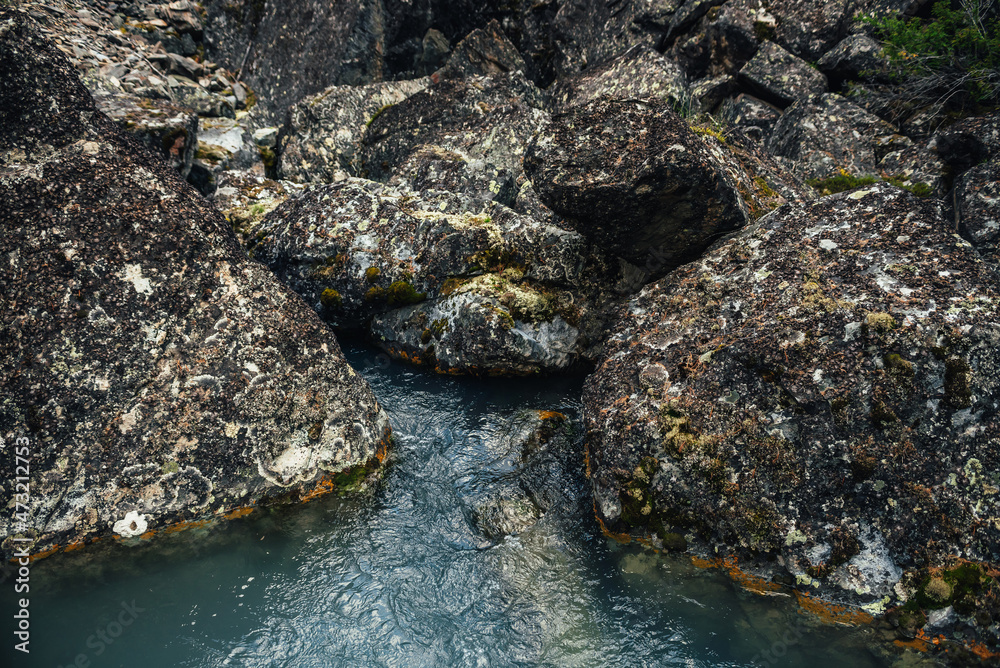 Scenic nature background of turquoise clear water stream among rocks with mosses and lichens. Atmospheric mountain landscape with mossy stones in transparent mountain creek. Beautiful mountain stream.