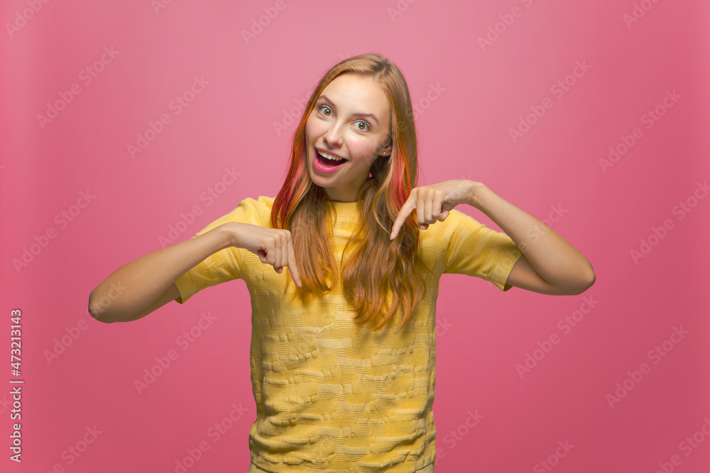 Cool offer. Surprised happy young girl pointing down. Excited woman blogger showing link to subscribe on pink background Cool offer. Surprised happy young girl pointing down. Excited woman blogger showing link to subscribe on pink background