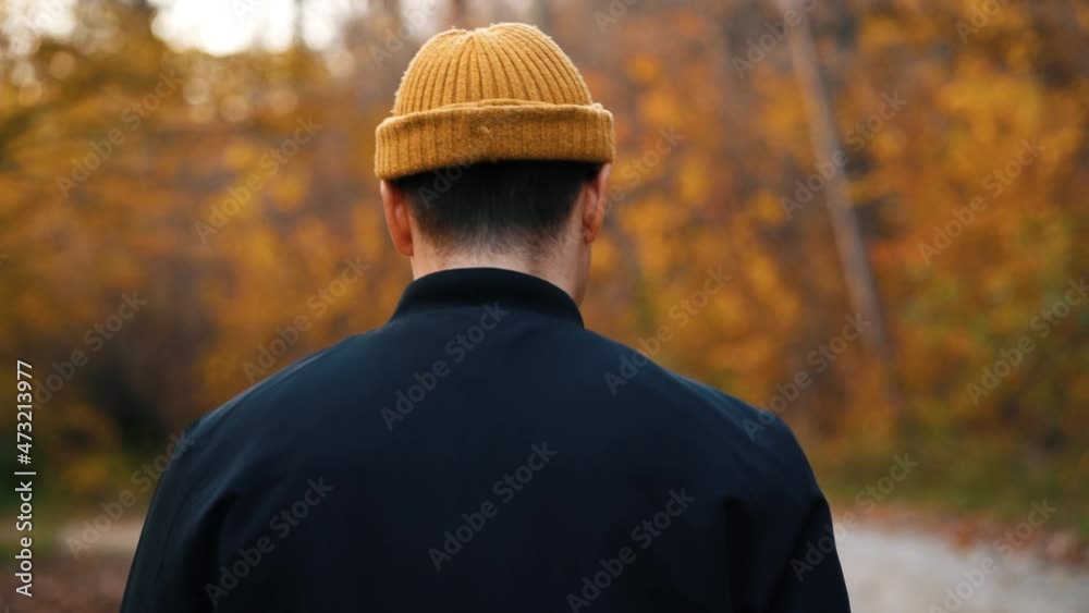 One unrecognizable young man wear black jacket, yellow hat walk along the path in wonderful forest with yellow leaves on trees. Blurred background. Close up back view. Autumn. Outdoor. One unrecognizable young man wear black jacket, yellow hat walk along the path in wonderful forest with yellow leaves on trees. Blurred background. Close up back view. Autumn. Outdoor.